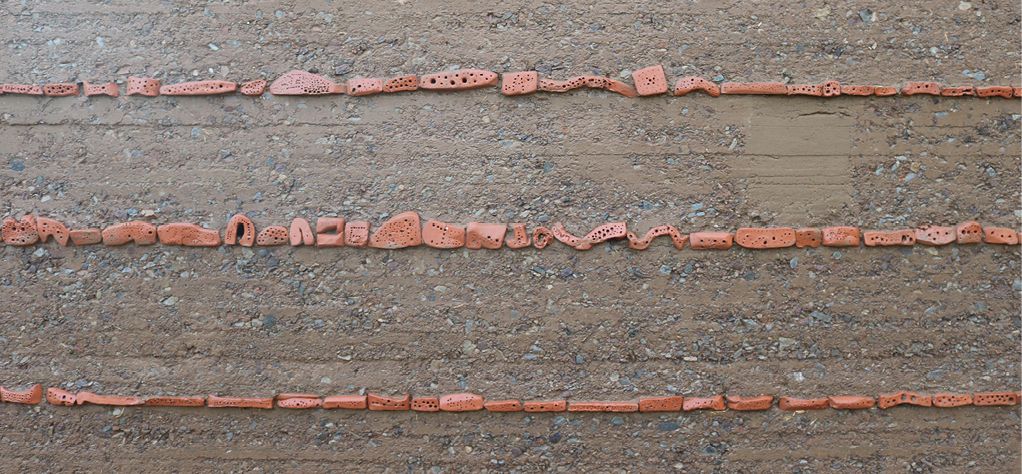 Bild 14 Bienensteine aus schwach gebranntem Ton in Stampflehm (Testwand in Nebelin); die primäre, erprobte Funktion dieser Bienensteine ist, bei Regen als Erosionsbremsen die Fließgeschwindigkeit von an der Wand herablaufendem Wasser zu reduzieren Quelle: Ute Reeh